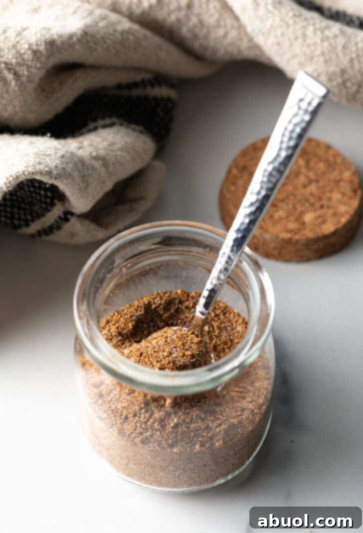 Small glass jar with pork chop seasoning and a metal spoon.