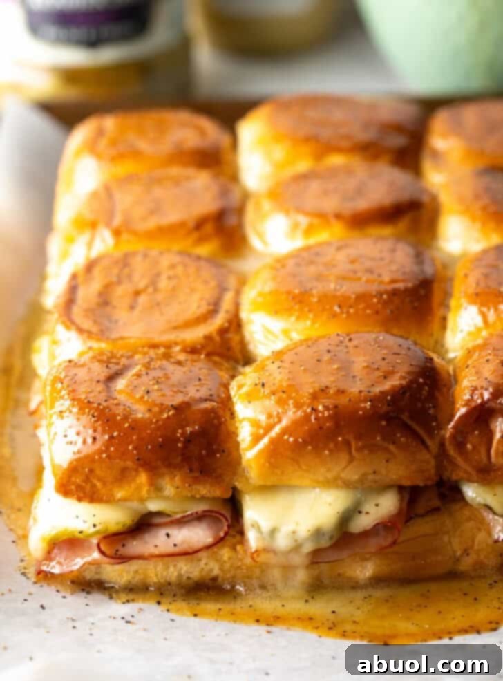 Sweet Hawaiian Bites 2 A dozen golden-brown King's Hawaiian ham and cheese sliders arranged on a rustic wooden board, garnished with fresh herbs, ready to be served.