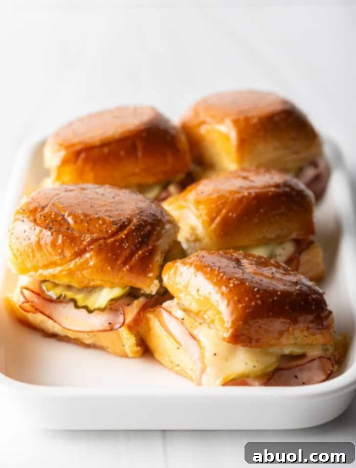 Sweet Hawaiian Bites 12 Another view of five King's Hawaiian ham and cheese sliders presented on a clean white rectangular serving plate, highlighting their appetizing appearance.