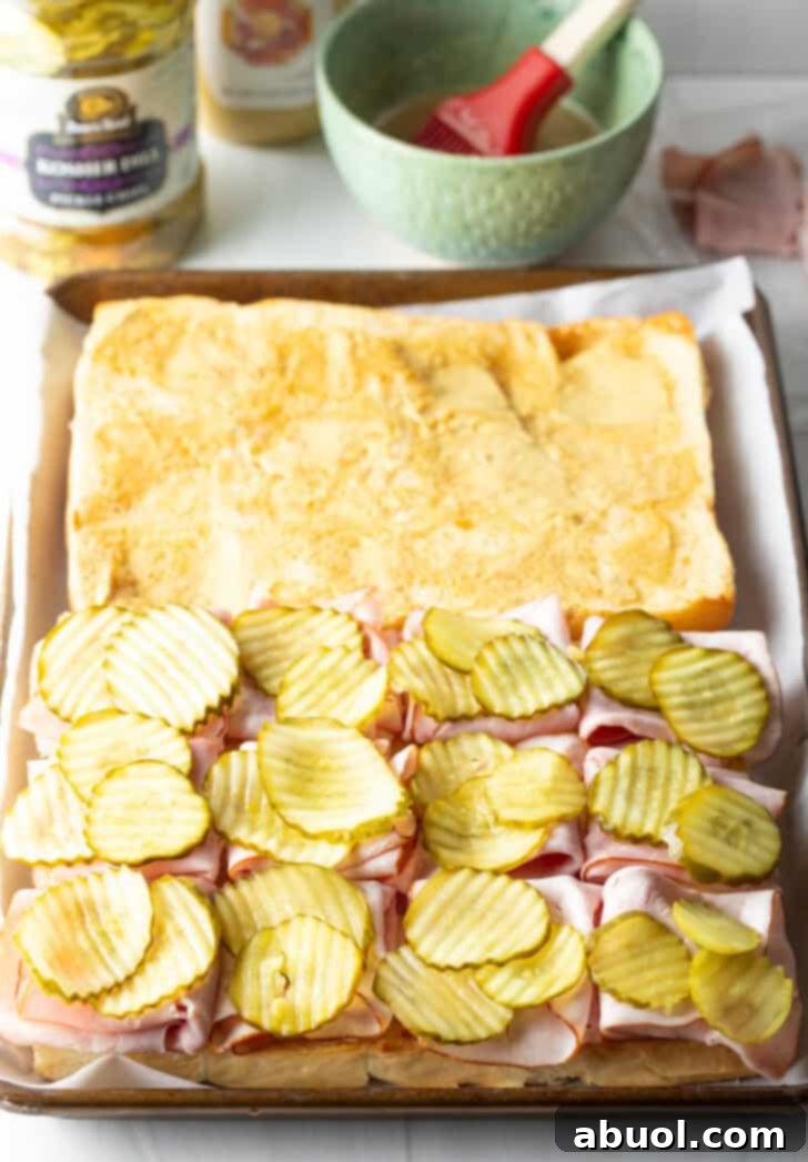 Sweet Hawaiian Bites 9 Continuing the assembly of King's Hawaiian rolls with crunchy dill pickles and more squares of cheese placed on top of the ham layer.