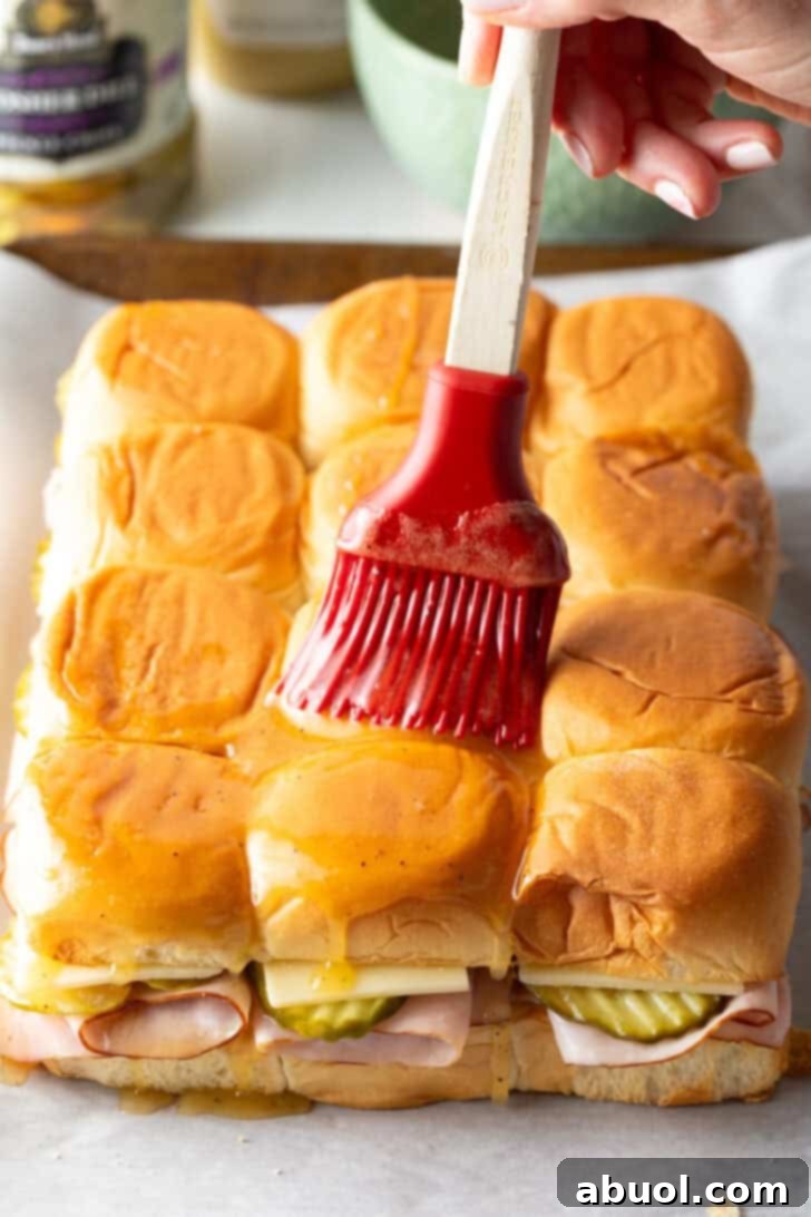 Sweet Hawaiian Bites 10 A red silicone brush applying the final honey butter glaze generously over the top of a dozen assembled sliders before baking.