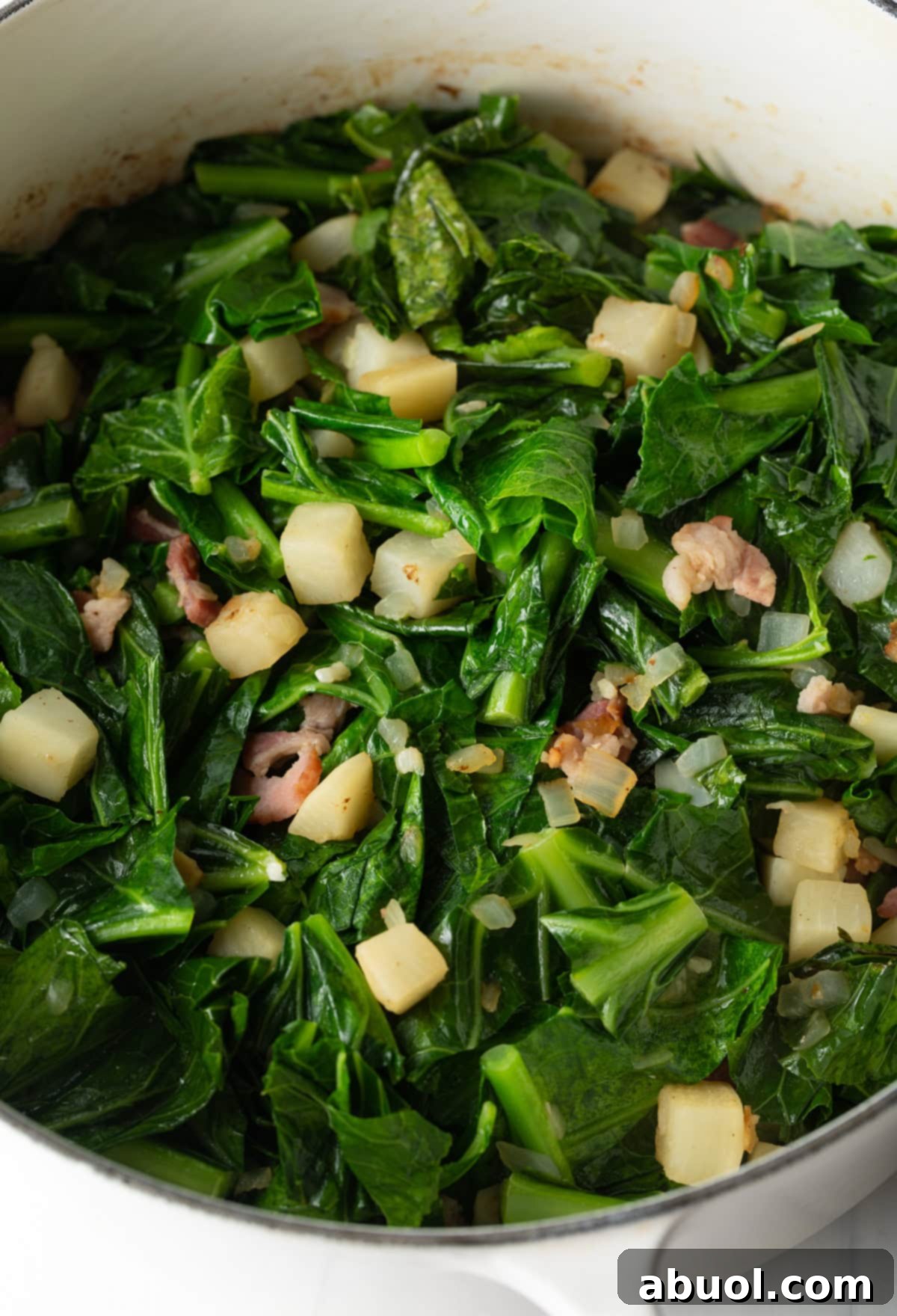 A generous pot of collard greens simmering in a Dutch oven, enriched with pieces of parsnip and bacon, showcasing the cooking process.