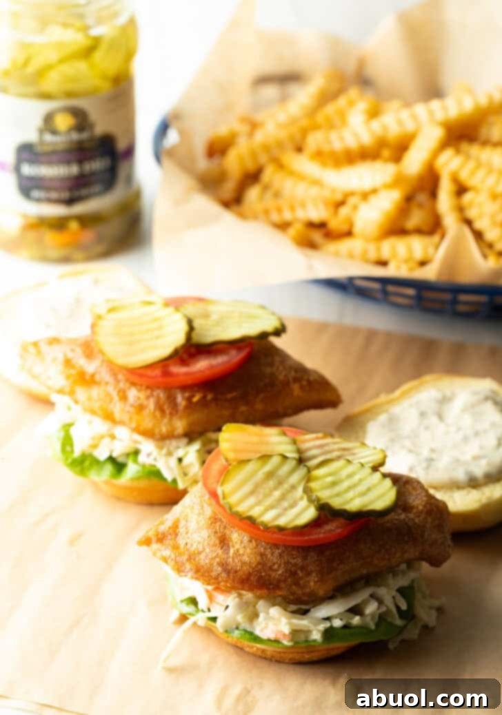 Two open face fried fish sandwiches, each topped with a slice of tomato and pickle slices.