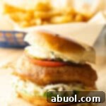 Battered and fried fish sandwich on a bun with coleslaw, tartar sauce, and a slice of tomato.