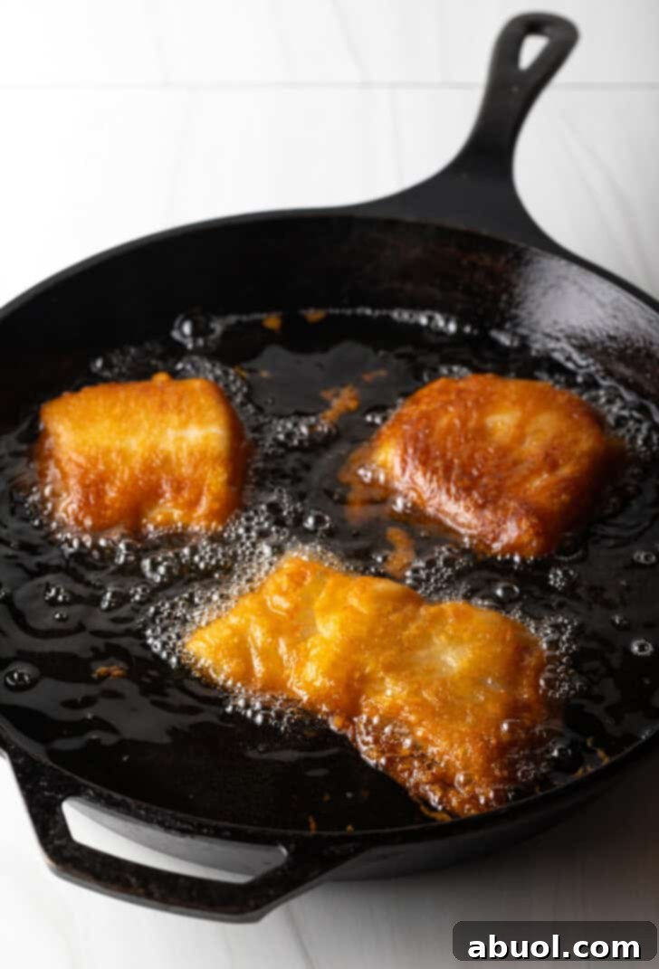 Frying pieces of breaded fish in a cast iron skillet.