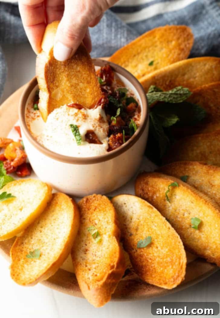 Hand dipping a slice of toasted baguette into a bowl of creamy whipped feta dip.