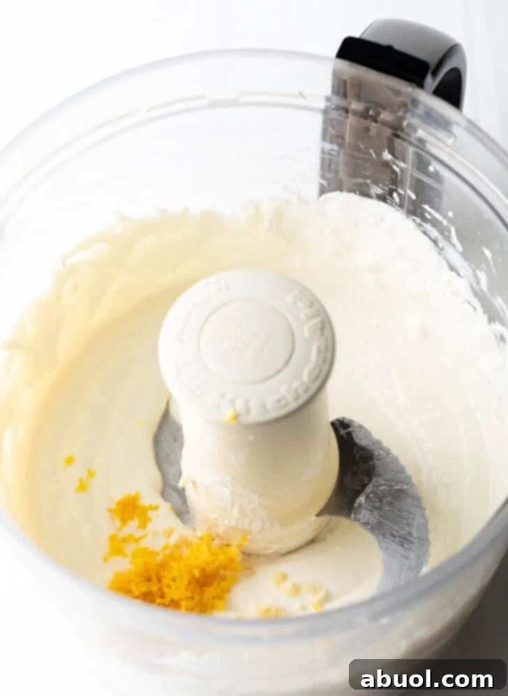 Adding lemon zest to creamy cheese and sour cream in a food processor.
