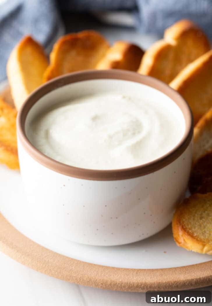 Creamy feta dip in a white bowl, on a plate with slices of toasted bread.
