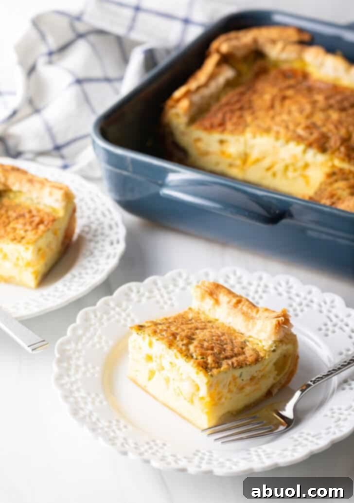 A square of delicious egg casserole rests on a white plate with a fork, while in the softly blurred background, the full baking dish of casserole awaits.