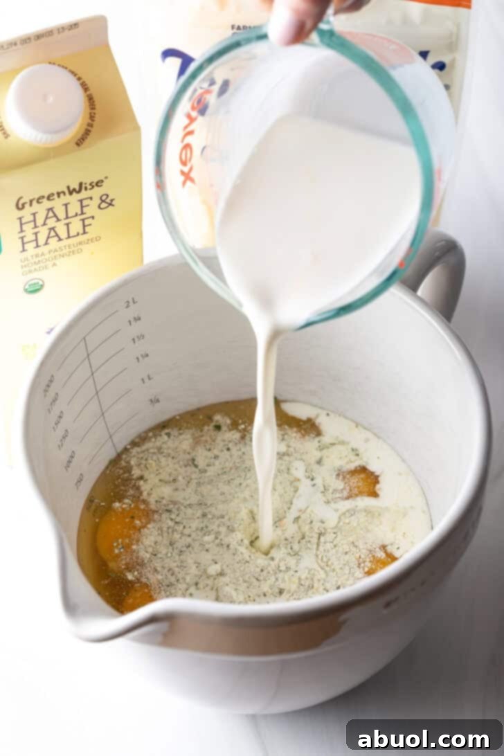 Milk is being poured from a glass measuring cup into a large white mixing pitcher already containing cracked eggs.