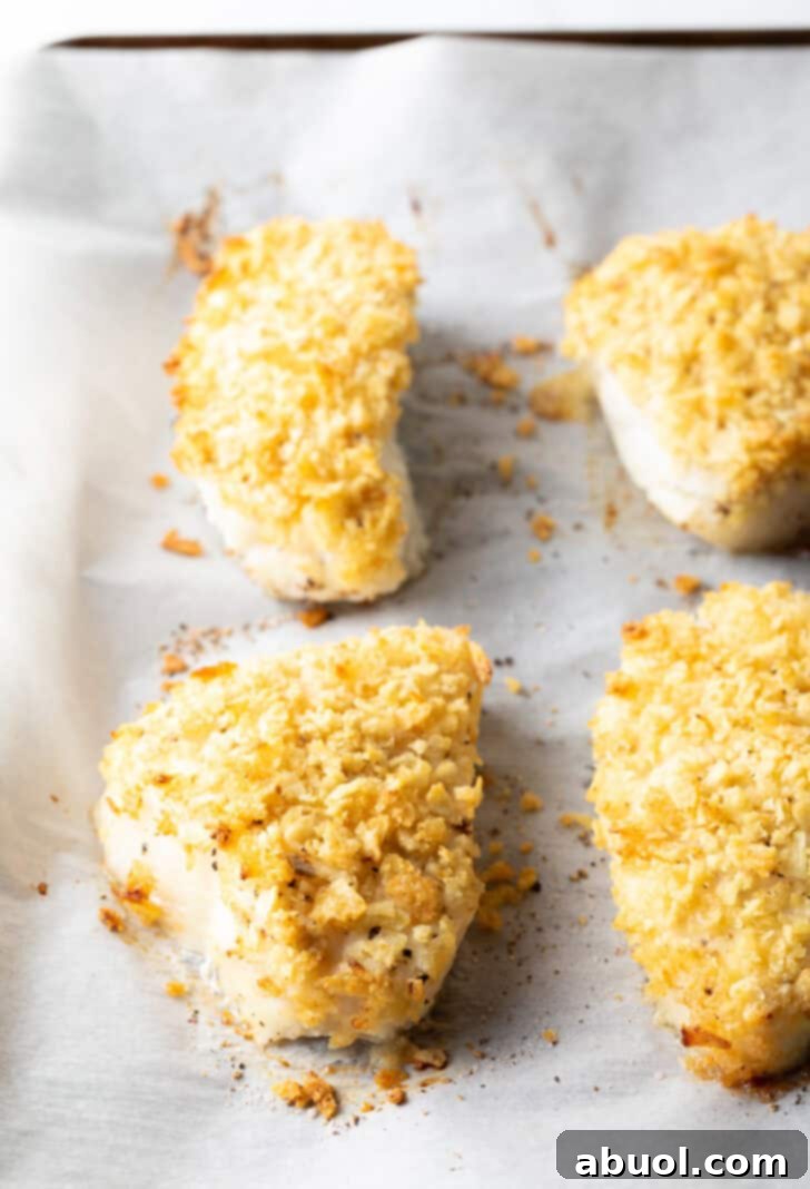 A close-up view of four baked fish fillets, showcasing their perfectly golden and crispy potato chip crusts, freshly removed from the oven and ready to be served.