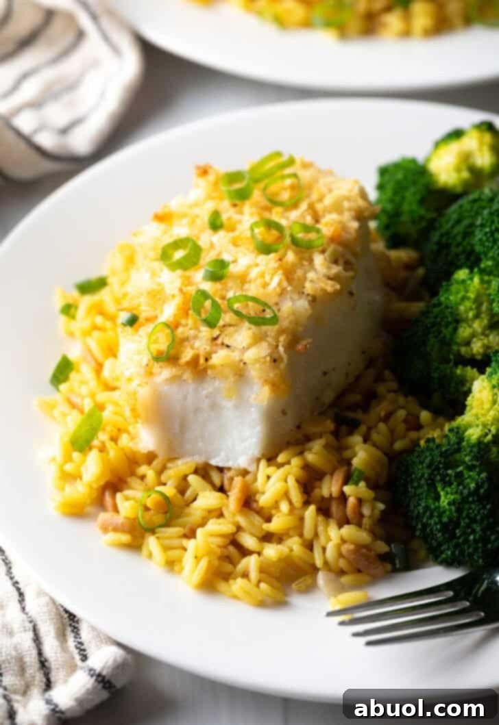 A beautifully composed close-up of the star dish: potato chip crusted baked sea bass, expertly paired with fluffy yellow rice and verdant cooked broccoli florets on a pristine white plate, invitingly ready to be served.