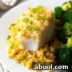 Potato chip crusted and baked bass on a plate with yellow rice and cooked broccoli.