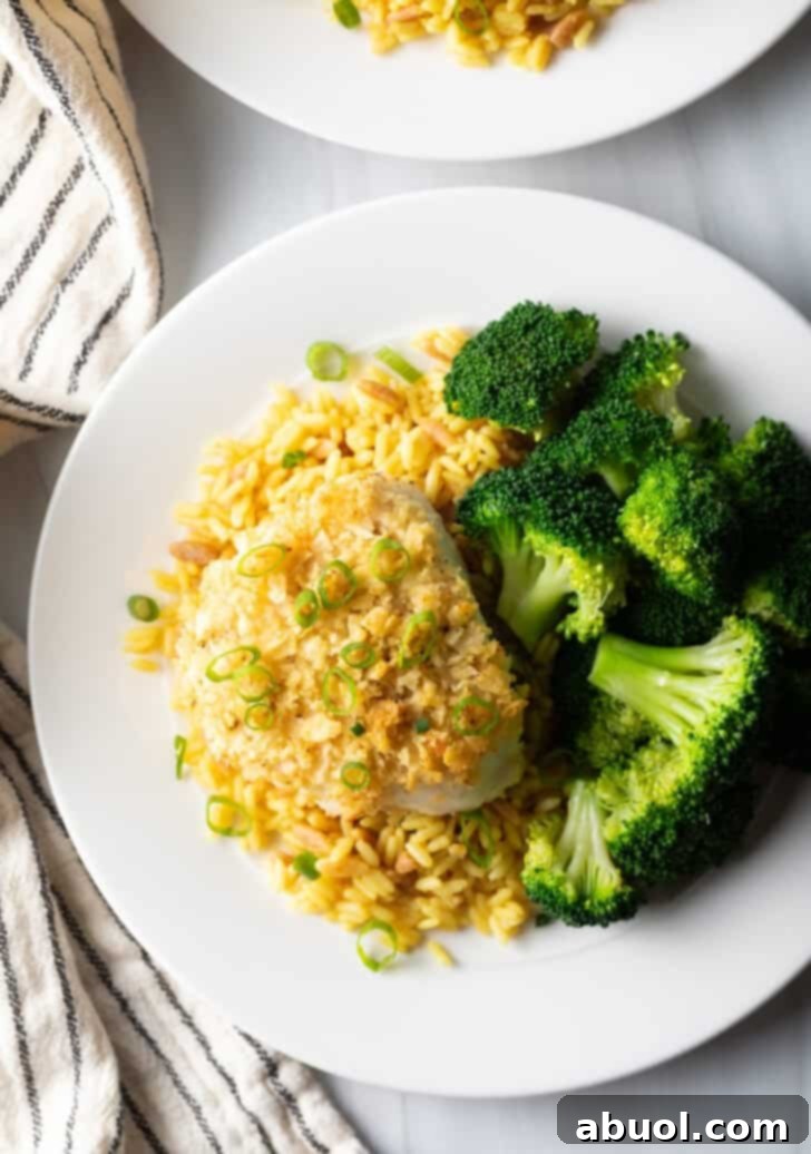 An inviting overhead view of a plate featuring the potato chip crusted baked sea bass, complemented by a serving of bright yellow rice and perfectly cooked broccoli florets.