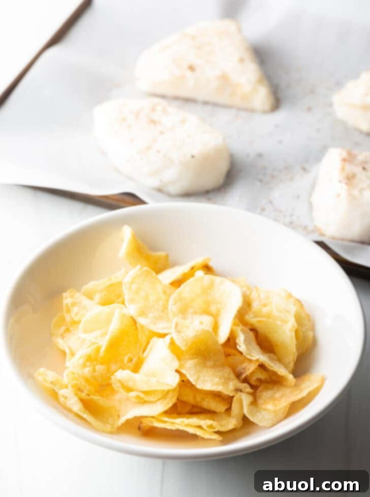 A crisp white bowl overflowing with whole potato chips, positioned in front of four raw bass fillets, signifying the readiness of ingredients for the next step.