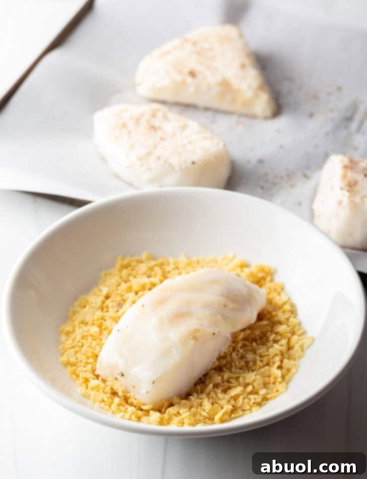 A raw sea bass fillet being gently pressed into a bowl filled with finely crushed potato chips, ensuring an even and flavorful crust.