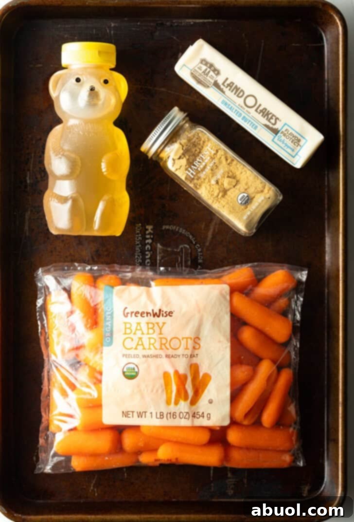 Top down view of ingredients: Bag of baby carrots, bear bottle of honey, garlic powder jar, and stick of butter.