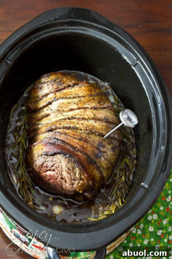 Crock Pot Beef Tenderloin with bacon wrapped around beef and a meat thermometer inserted for perfect doneness