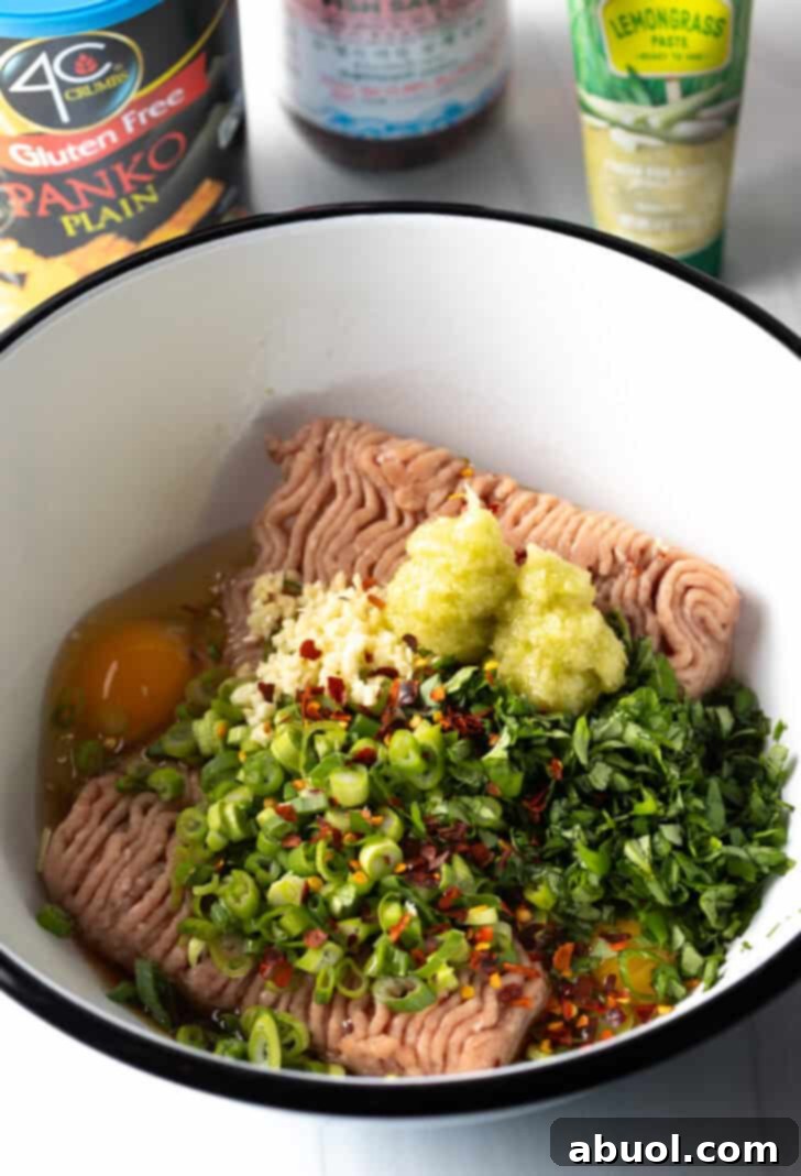 A white mixing bowl containing ground turkey, fragrant lemongrass, an egg, and fresh basil, ready to be combined.