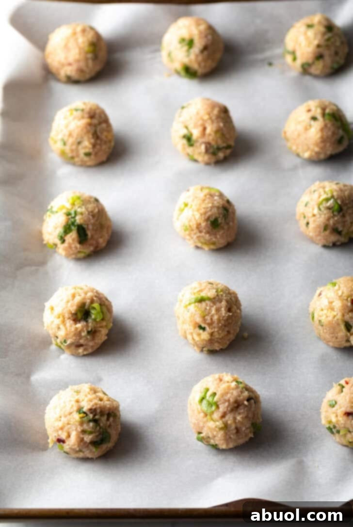 Fifteen raw, perfectly shaped turkey meatballs neatly arranged on a parchment-lined baking sheet, ready for the oven.