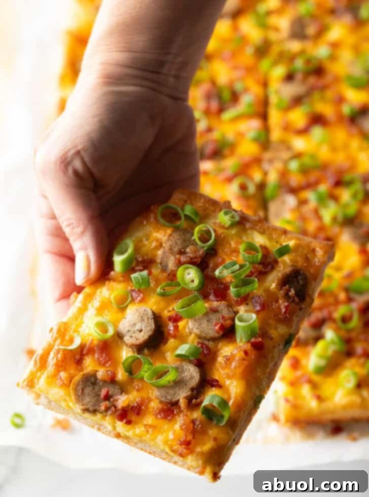 A rectangular baking sheet tray presenting a delectable breakfast pizza, loaded with cheese, sausage, and green onions. The pizza has been cut into 8 rectangles, and a hand is reaching in to pull away one inviting slice.