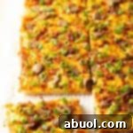 Rectangle baking sheet tray with breakfast pizza, loaded with cheese, sausage, and green onions. The pizza has been cut into 8 rectangles, with one piece pulled away.