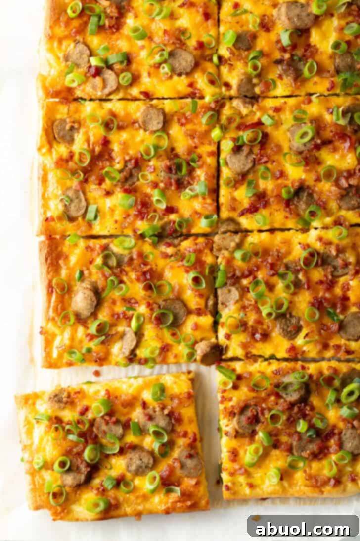 A rectangular baking sheet tray filled with a scrumptious breakfast pizza, generously topped with melted cheese, savory sausage, and fresh green onions. The pizza is clearly cut into 8 rectangular pieces, with one slice slightly pulled away from the main pie.