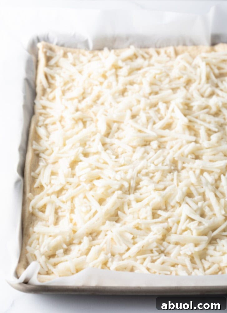 Close-up of shredded mozzarella cheese generously spread over an unbaked rectangular pizza crust.