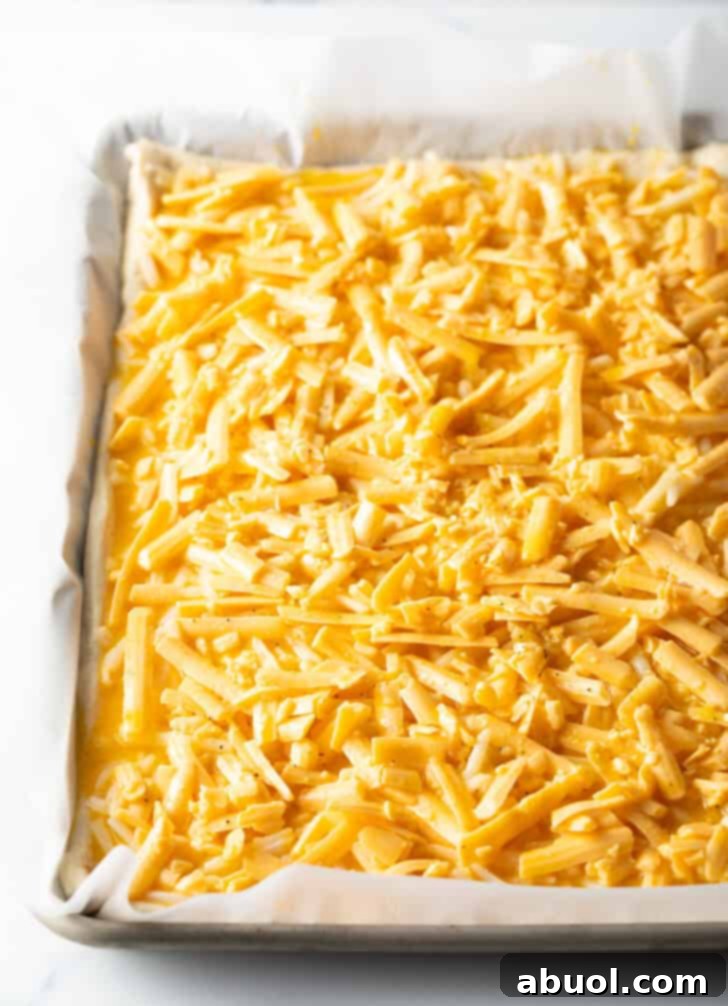 Close-up of shredded cheddar cheese evenly distributed over an unbaked rectangular pizza base.