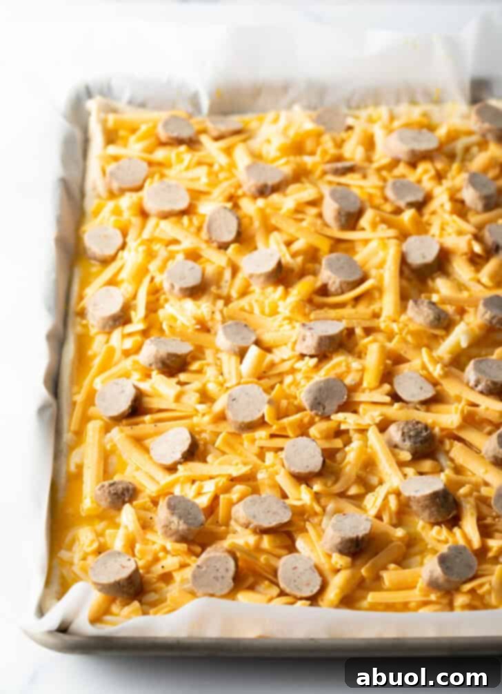 Shredded mozzarella cheese and neatly sliced breakfast sausage pieces topping an unbaked rectangular pizza crust, ready for the oven.