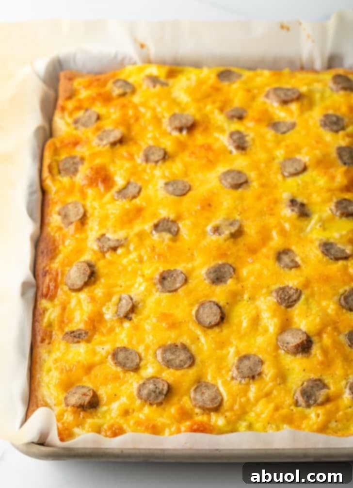 A perfectly baked rectangular pizza, golden brown, with melted cheeses and glistening sausage slices visible on top.
