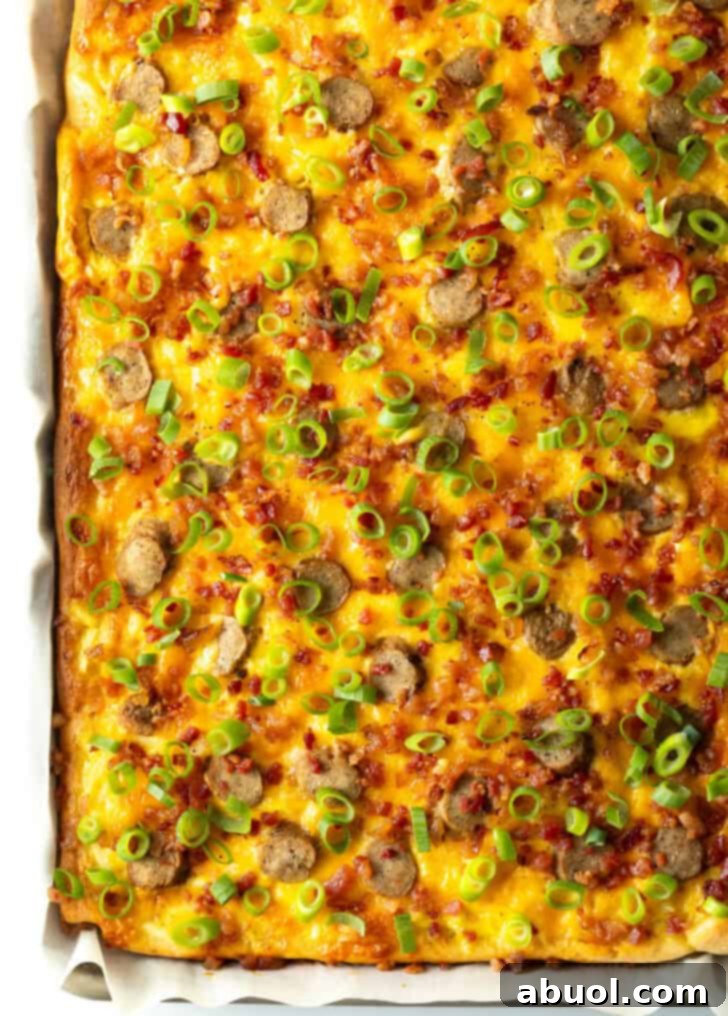 A full view of the rectangular baking sheet tray, holding a fully cooked breakfast pizza adorned with cheese, sausage, and green onions.