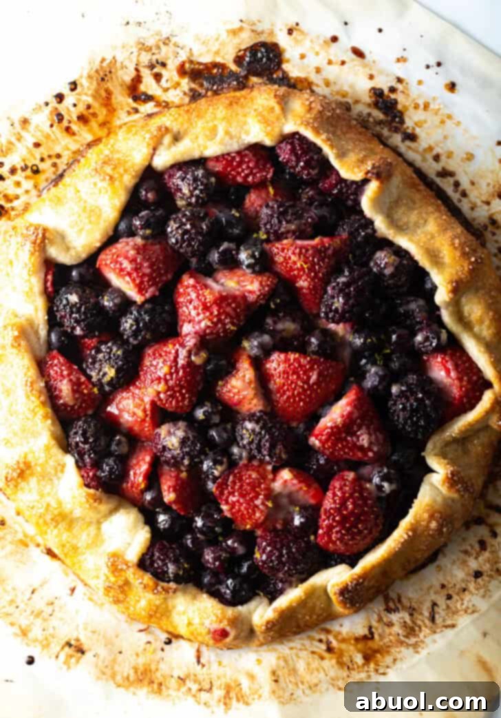 Top down view of a beautifully baked crostata, generously filled with glistening blueberries, blackberries, and strawberries, showcasing its rustic charm.