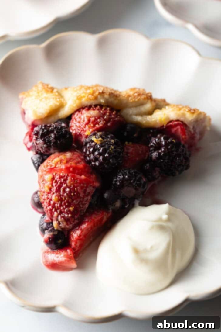 A perfectly portioned slice of berry crostata, showcasing its rich fruit filling and golden crust, presented on a white plate with a generous scoop of creamy ricotta topping on the side.