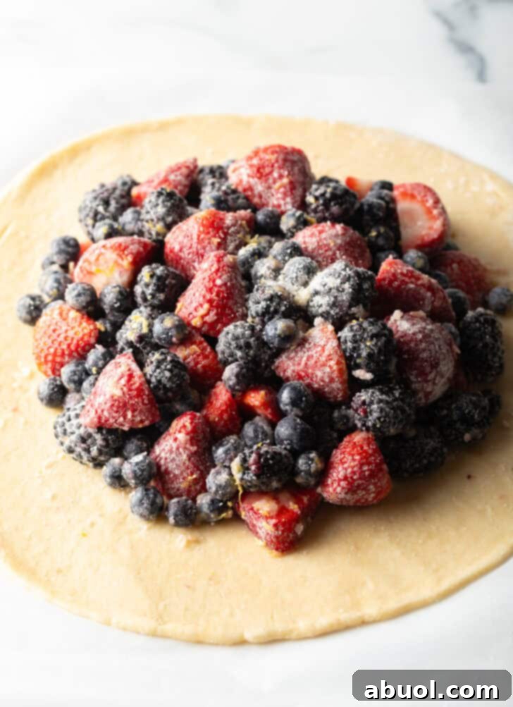 An open pie dough crust generously loaded with a vibrant mixture of strawberries, blueberries, and blackberries, ready for folding.