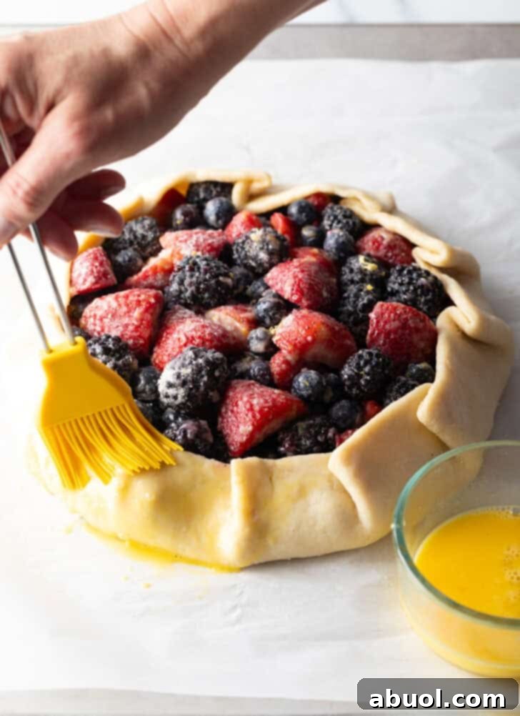 A hand expertly brushing the exposed outside edges of the berry crostata with an egg wash before baking.