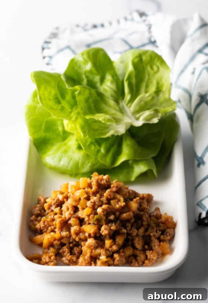 A white rectangle plate artfully arranged with a stack of fresh butter lettuce leaves and a generous pile of seasoned ground chicken filling, ready for assembly.