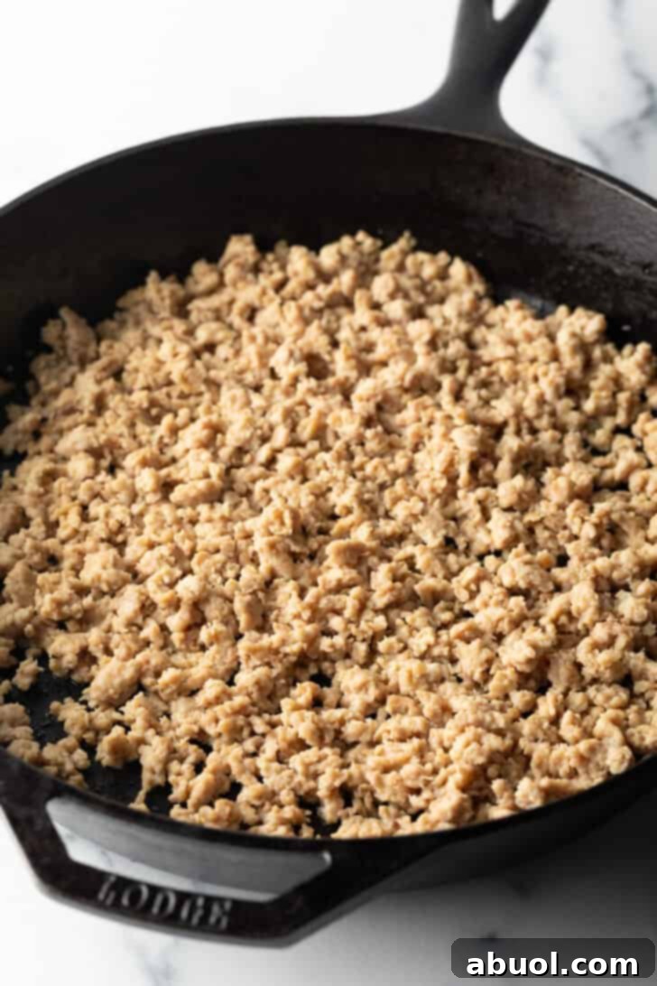 Ground chicken sizzling and browning in a cast iron skillet, being broken apart with a wooden spoon.