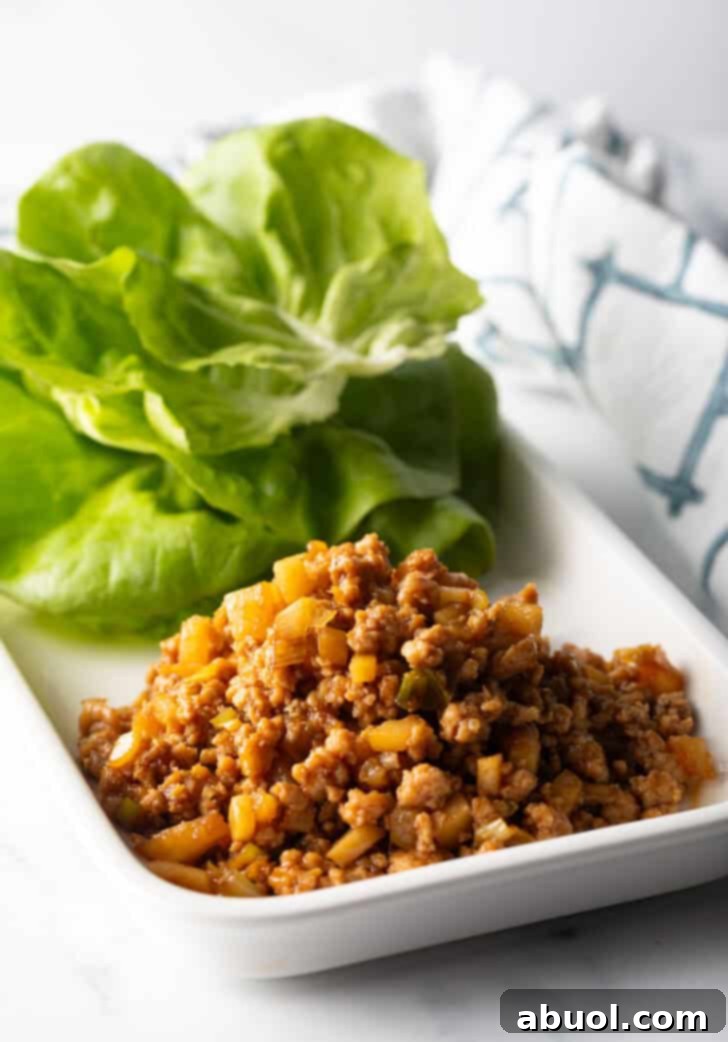 A white rectangle plate with a neat stack of crisp butter lettuce leaves beside a mound of the savory ground chicken filling, prepared for wrapping.
