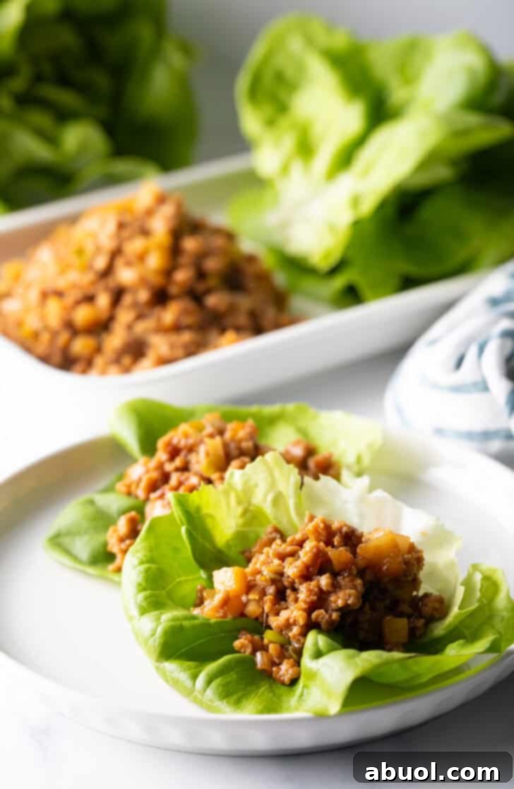 Two enticing PF Chang copycat lettuce wraps, generously filled with savory ground chicken meat and fresh garnishes, arranged on a pristine white round plate, promising a delightful culinary experience.