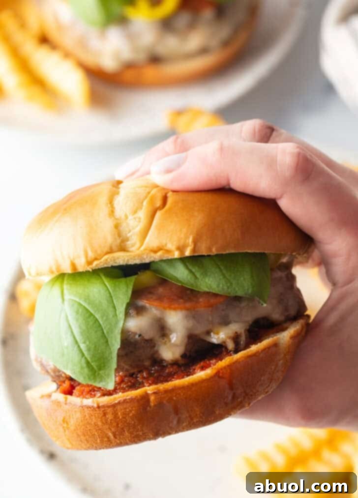A hand confidently holding a perfectly assembled Italian pizza cheeseburger, showcasing its layers, ready to be enjoyed.
