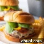 Pizza burger on a white and black speckled plate, with a pile of crinkle cut french fries.