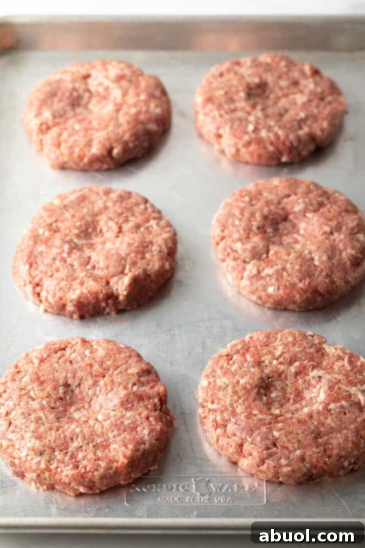 Six raw hamburger patties neatly arranged on a baking sheet, expertly formed and ready for cooking.