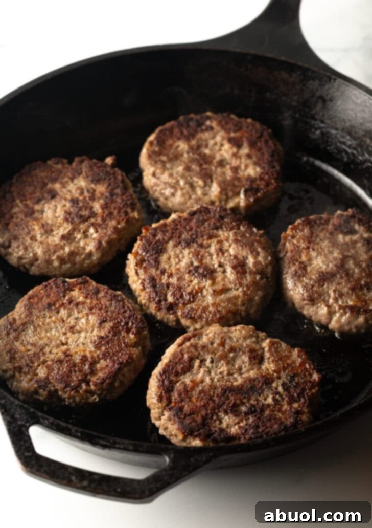 Six hamburgers sizzling and cooking to perfection in a large cast-iron skillet, developing a beautiful, savory crust.