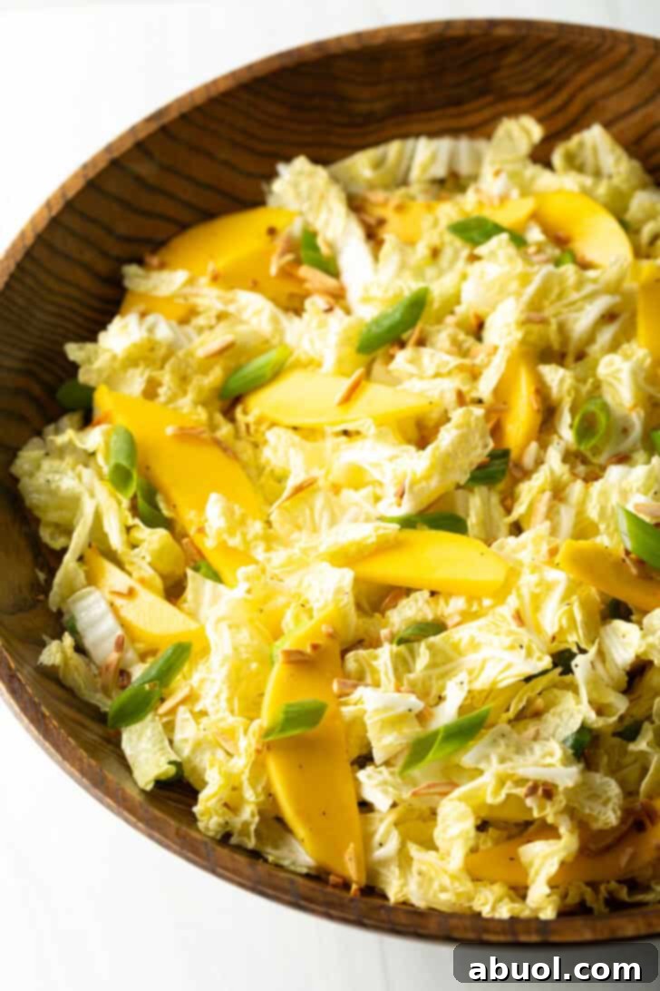 Top down view wood bowl with green napa cabbage, mango slices, and green onions, showcasing the fresh ingredients.