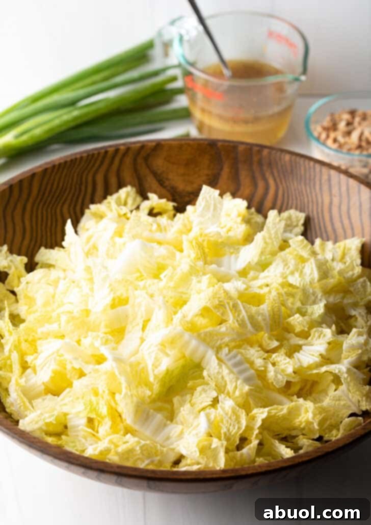 Shredded napa cabbage meticulously piled in a rustic wood bowl, forming the fresh base of the salad.