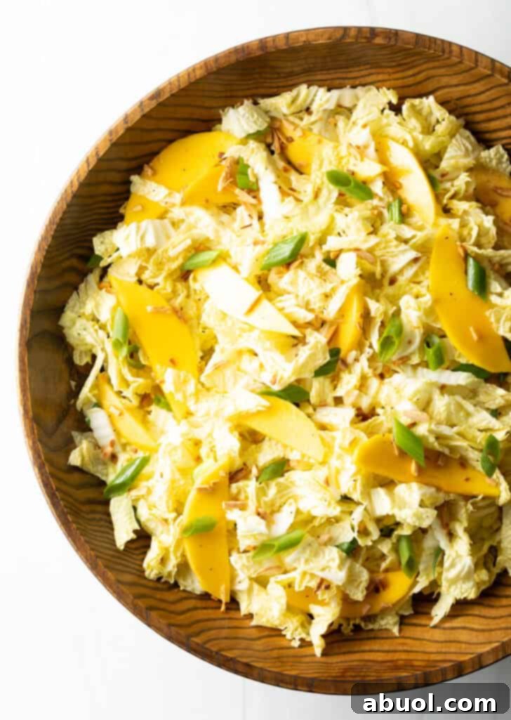 Top down view of a rustic wood bowl overflowing with vibrant green napa cabbage, luscious mango slices, and fresh green onions, expertly tossed and ready to be savored.