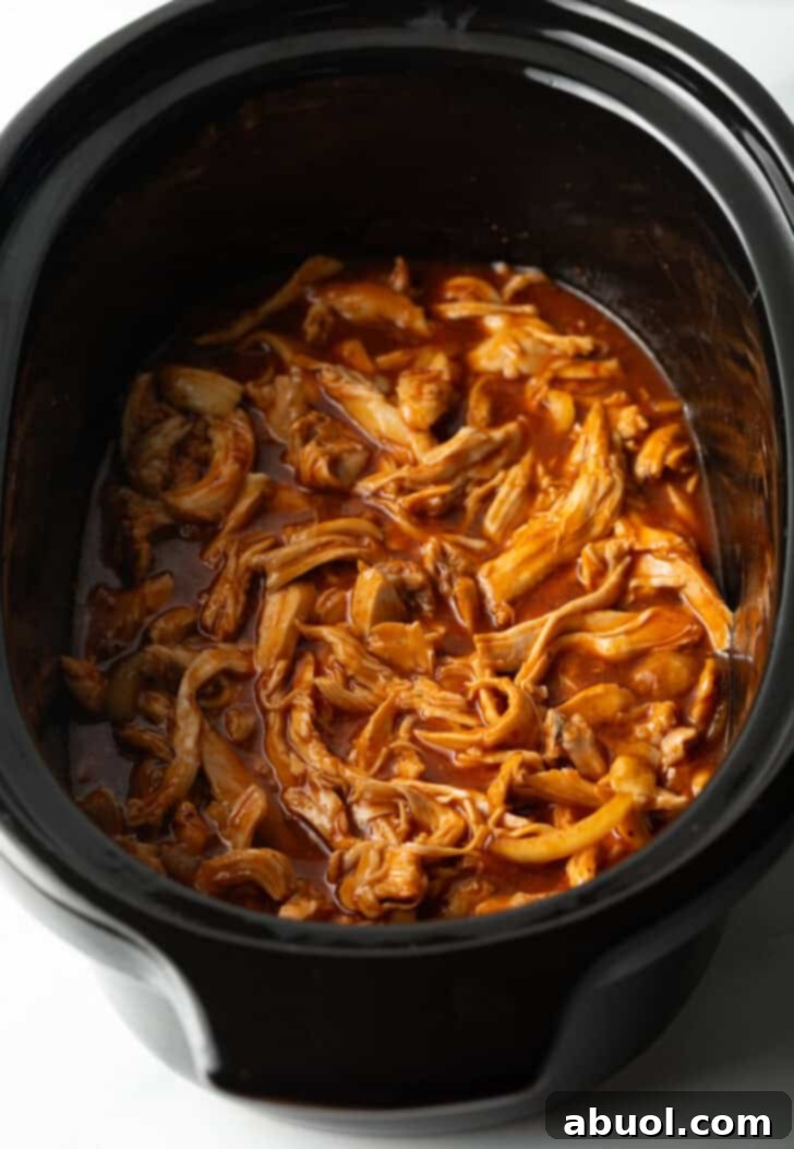 Perfectly shredded BBQ chicken, glistening with rich barbecue sauce, resting inside a slow cooker after hours of cooking.