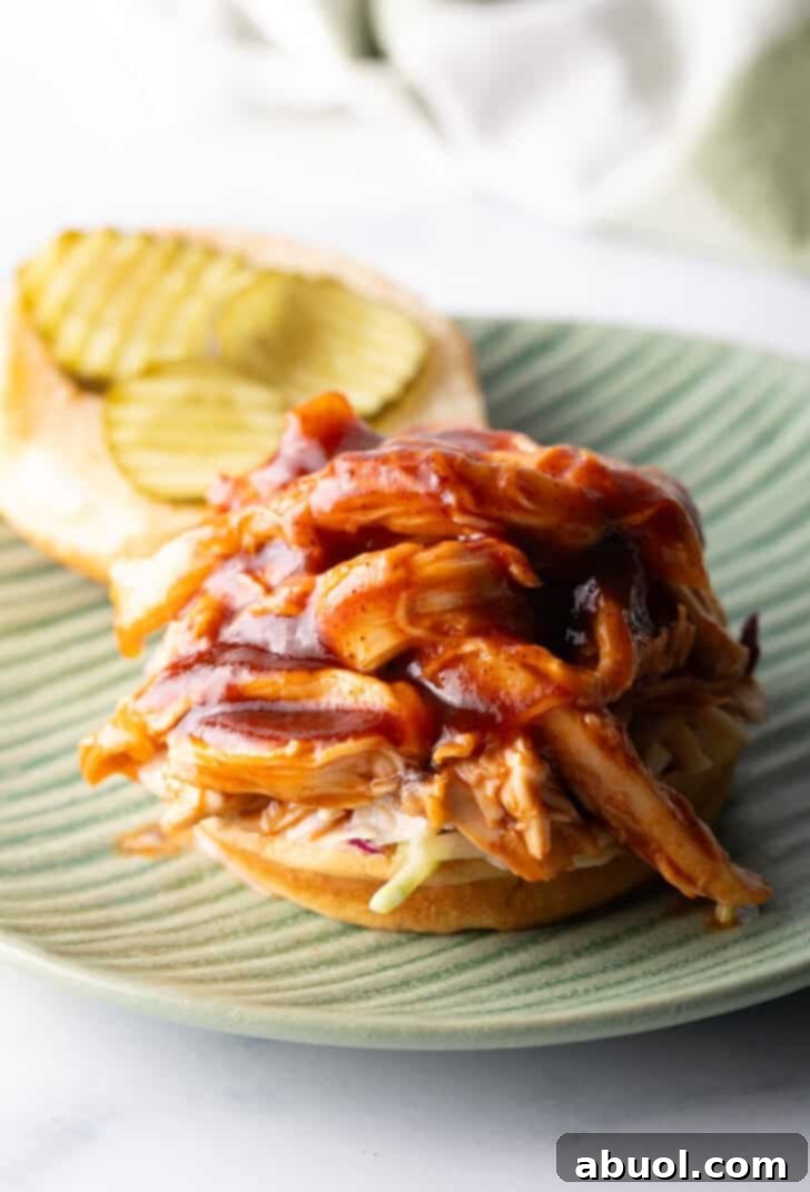 An open-faced pulled barbecue chicken sandwich, generously piled high with juicy chicken on a toasted hamburger bun, ready to be enjoyed.