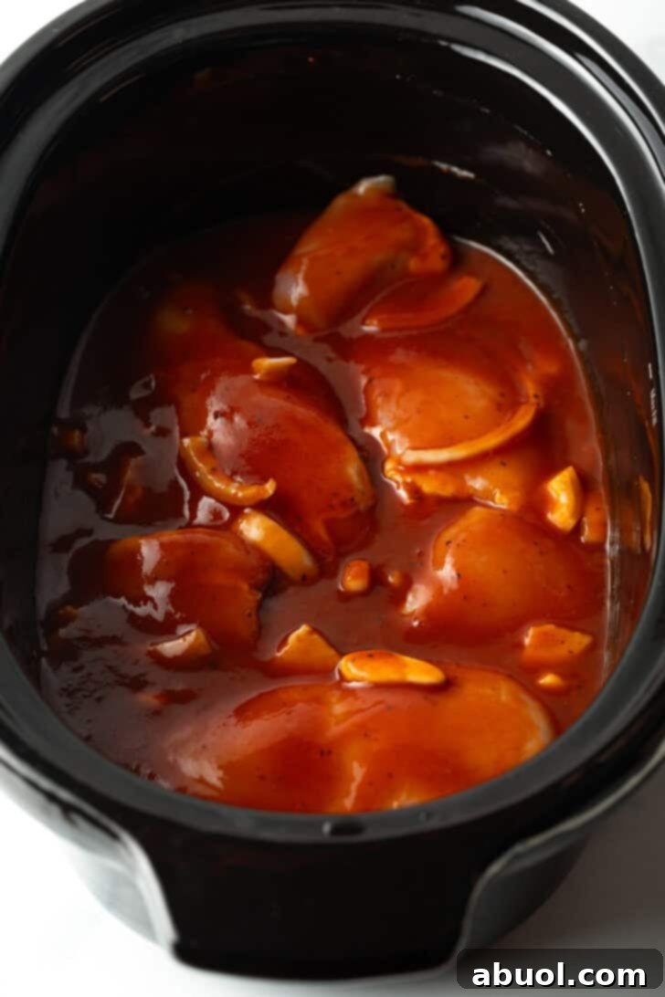 Chicken thighs nested in rich barbecue sauce within the crockpot, beautifully coated and ready for the slow cooking process.